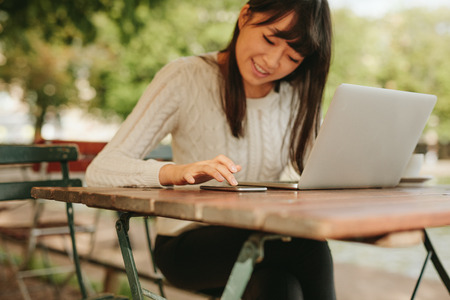 Image of young asian woman sitting at a table with laptop and using ...