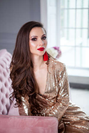Portrait of beautiful young woman with makeup in fashion clothes.Golden  dress in paetkas, trendy red earrings, hairstyle and red lips - Stock Image  - Everypixel