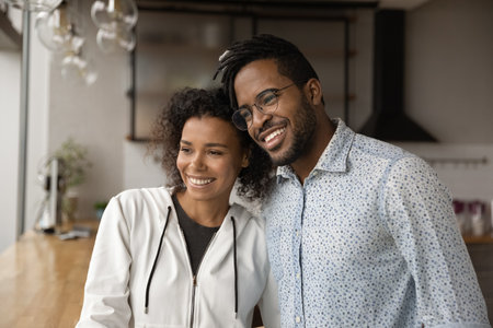 Smiling millennial African American couple hug look in distance ...