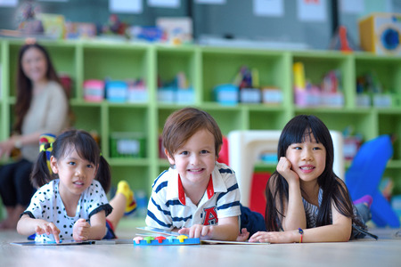 group of international kids in preschool enjoy reading books with teacher watching in back ground