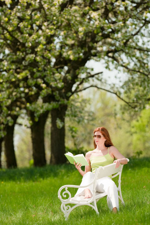 Red hair woman reading book on white bench in a meadow; shallow DOF ...