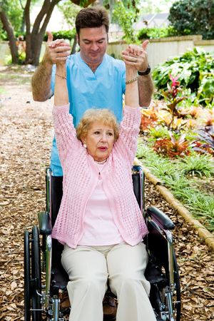 Physical therapist helping a disabled senior woman to regain mobility in her upper limbs.