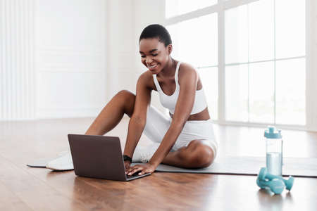 Smiling young black woman sitting on yoga mat using laptop - Stock ...