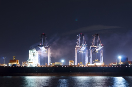 Container Cargo ship with working crane bridge in shipyard at dusk ...
