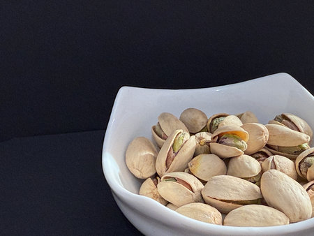 Pistachios in a white bowl. Bowl of pistachios on dark background.