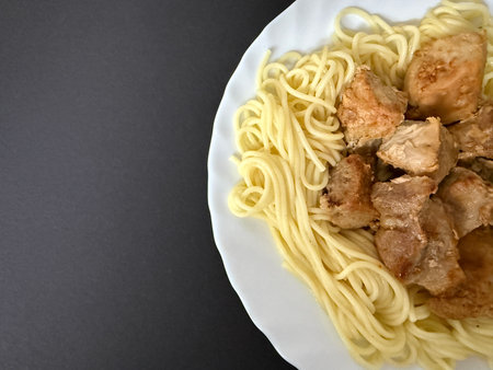 Close-up shot of spaghetti with fried pork pieces on a white plate. Cooking delicious food at home.の写真素材