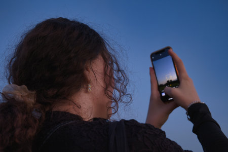 A young woman with curly hair is taking a photo with her mobile phone.