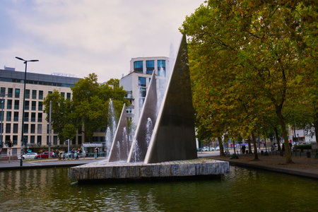 Urban fountain with modern sculpture and green trees near business buildings in city parkの写真素材