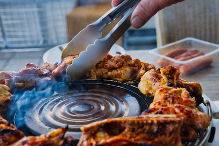 grilled chicken on the barbecue grill with tongs, closeupの写真素材