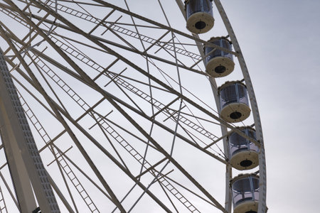 A close-up view of a Ferris wheel shows its frame and cabins against a cloudy sky at a fair.