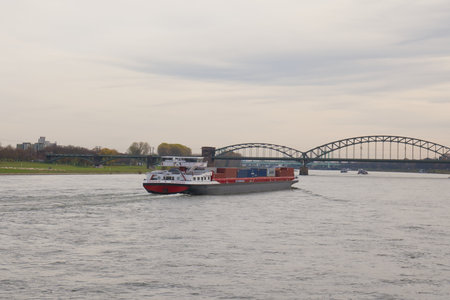 Cargo ship travels along the river while a bridge stands in the background during an overcast day.の写真素材