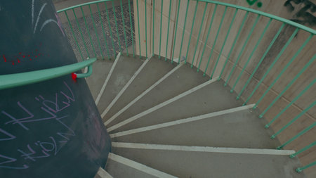 A view of a spiral staircase descending into an urban area with graffiti on the walls and interesting textures.の写真素材