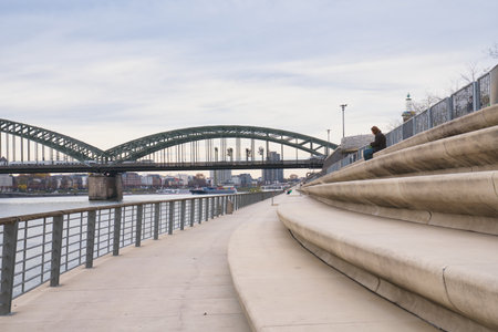 A person sits quietly on steps by the riverbank, overlooking the water and a bridge on a peaceful...