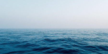 Gentle waves roll across the calm ocean horizon, blending with a soft, clear sky in a minimalist scene.の素材