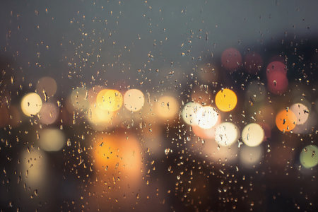Raindrops create a beautiful pattern on the window, softening the bright city lights outside during the evening.の素材