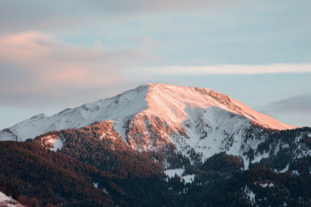 The sun casts a warm glow on the snow-capped mountain at dusk, highlighting its rugged beauty.の素材