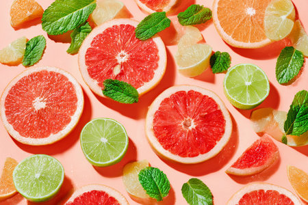 Freshly sliced citrus fruits and mint leaves are artistically arranged on a soft peach surface, ready for use.の素材