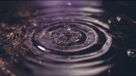 Water droplets fall softly, forming intricate ripple patterns in dark liquid, reflecting light beautifully.の素材