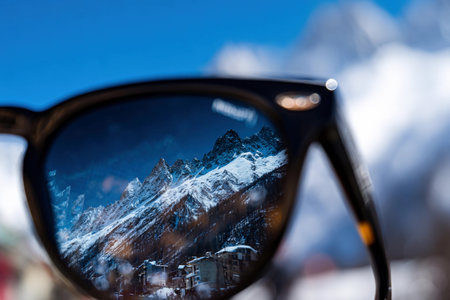 Sunglasses show a mountain range and blue sky, capturing the beauty of nature on a sunny day.の素材