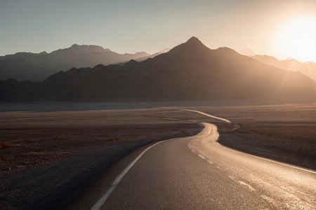 Straight road in the desert leads to mountains as soft light of sunrise begins to appear.の素材