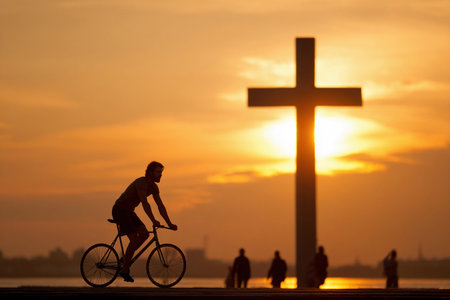 Christ is riding a fixie bike in Brooklyn at sunset with a large cross in the background.の素材