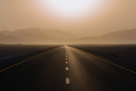 A straight road runs through the desert as the sun rises, illuminating the landscape.の素材