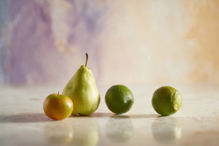 A group of fresh fruits including an apple, a pear, and two limes placed on a smooth surface.の素材