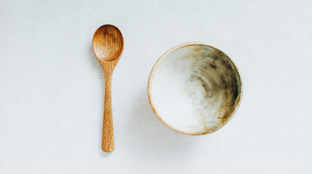 A wooden spoon rests next to a bowl on a clean white background for eating.の素材