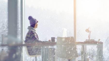 A businessperson sits in a quiet office focused on work while it snows outside the window.の素材