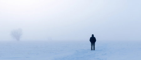 A person stands alone in an open snowy area with soft fog during winter time.の素材