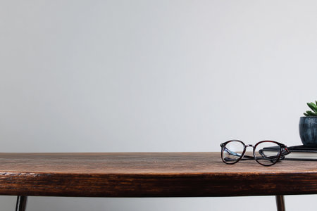 A desk holds a pair of eyeglasses, a small plant, and a notepad on a simple surface in neutral colors.の素材