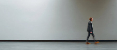 A person is moving slowly in a large, empty area with plain walls and floor in a neutral setting.の素材