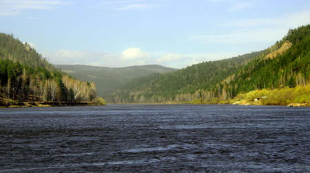 A wide river runs slowly towards the wooded mountains.の写真素材