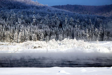 In the background, on the other bank of the river, conifer winter forest begins. Everything is simple, beautiful and expressive. In the foreground - mist rising from the water and fluffy snow.の写真素材