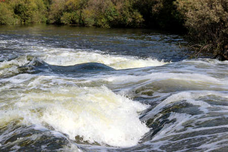 The mountain river flows over the rocks bubbling and foaming.の写真素材