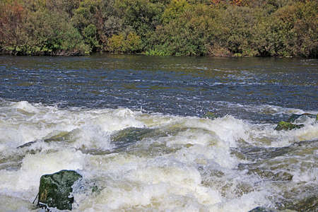 The mountain river flows over the rocks bubbling and foaming.の写真素材