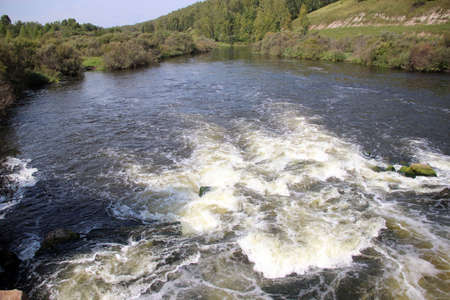The mountain river flows over the rocks bubbling and foaming.の写真素材