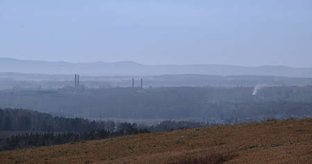 View from a hill on a hilly area in a blue haze. You can see the protruding pipes of factories and white smoke.の写真素材