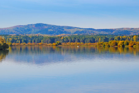 Amazing panoramic view of a wide-spreading river against the background of wooded mountains under a blue sky.の写真素材
