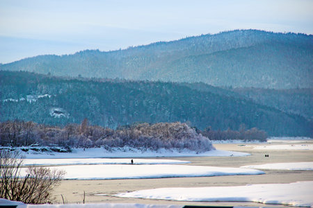 Winter landscape - the river runs between snowy shores and woody hills and fishermen are fishing.の写真素材