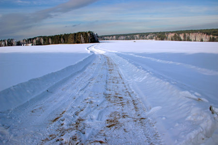 Beautiful scenery.  The winter road cuts deep into the snow and runs, curving and losing itself in the forest.の写真素材