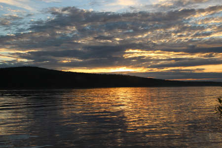 Evening sky over the river. Reflection of the sun in water. Twilight and the mountain silhouette backgroundsの写真素材