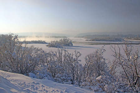 Winter landscape - river runs between snowy shores and woody hills.の写真素材