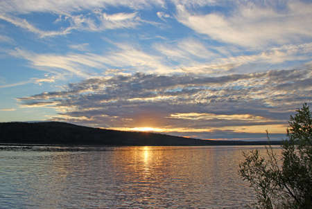Evening sky over the river. Reflection of the sun in water. Twilight and the mountain silhouette backgroundsの写真素材