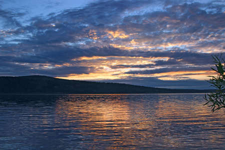 Dark blue sky with golden patches gloomy hangs over river water and its reflectionの写真素材