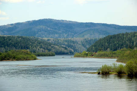 Amazing scene of the winding river and wooded mountain ahead. Several roofs and fishermen far away on the right shoreの写真素材