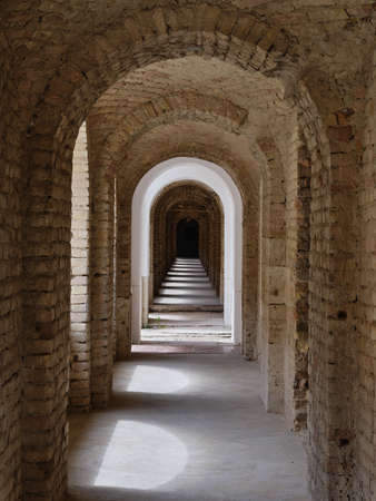 Arched brick corridor with shadows and daylight through the windows in the old fortress in...