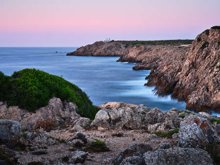 The rocky coast of Menorca island and the house at the end of the cliff, Spainの写真素材