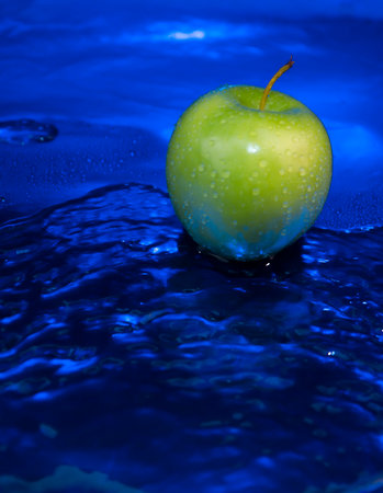 Green apple falling into the water with droplets on it. Blue background.の写真素材