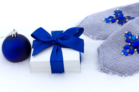 Gift in a box and blue gloves with rhinestones on the snow.の写真素材